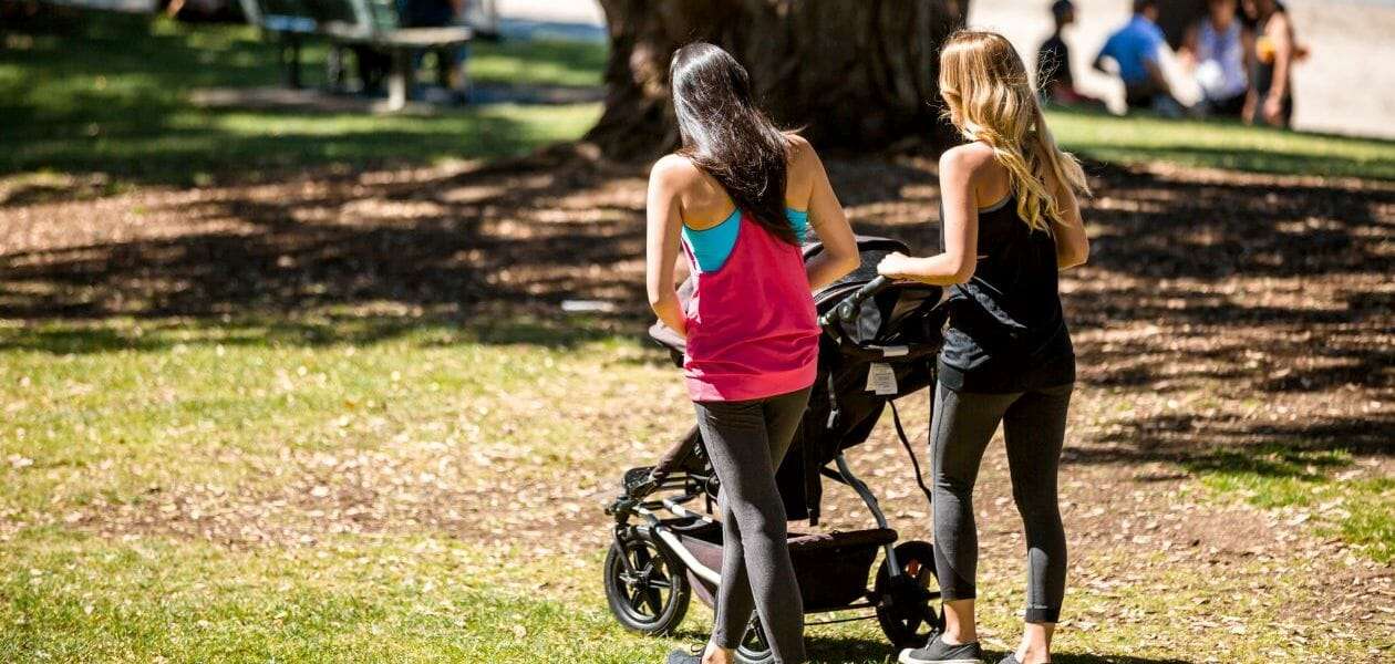 Two women walking a baby in a pram in a park