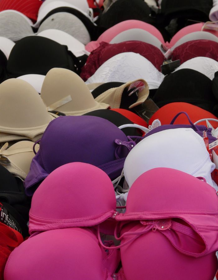 Collection of bras in pink, purple, black, white and nude piled together, showing poor bra storage.