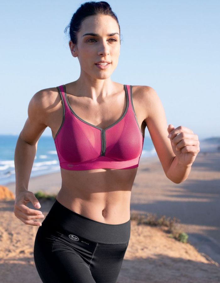 Woman running outdoors by the beach wearing a pink high-support sports bra designed for running and active movement.