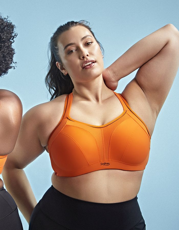 Woman wearing an orange high-support sports bra designed for large breasts, with full coverage cups and wide supportive straps.